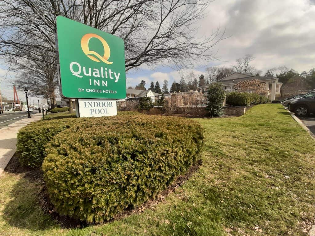 A green sign for Quality Inn hotel in Gettysburg sitting near shrubbery.