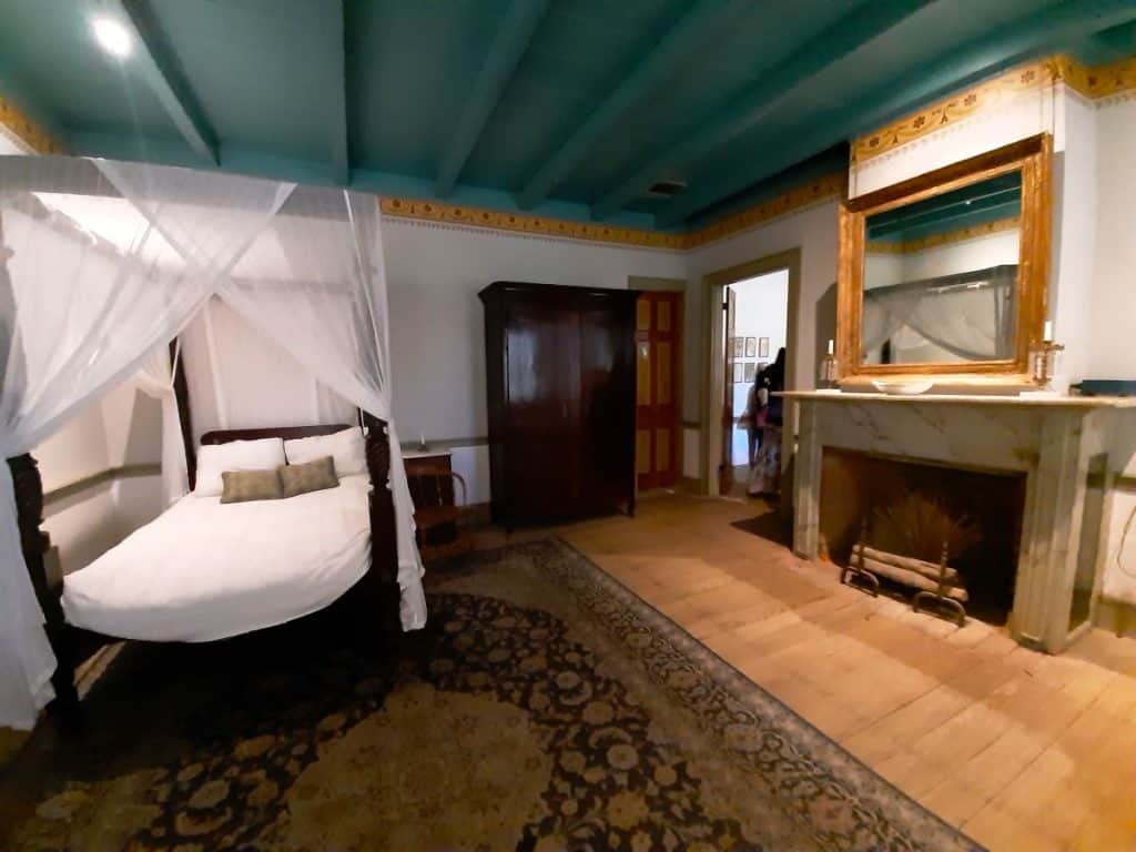 One of the bedrooms at Laura Plantation, shows a white bed with canopy, wooden floors and fireplace.