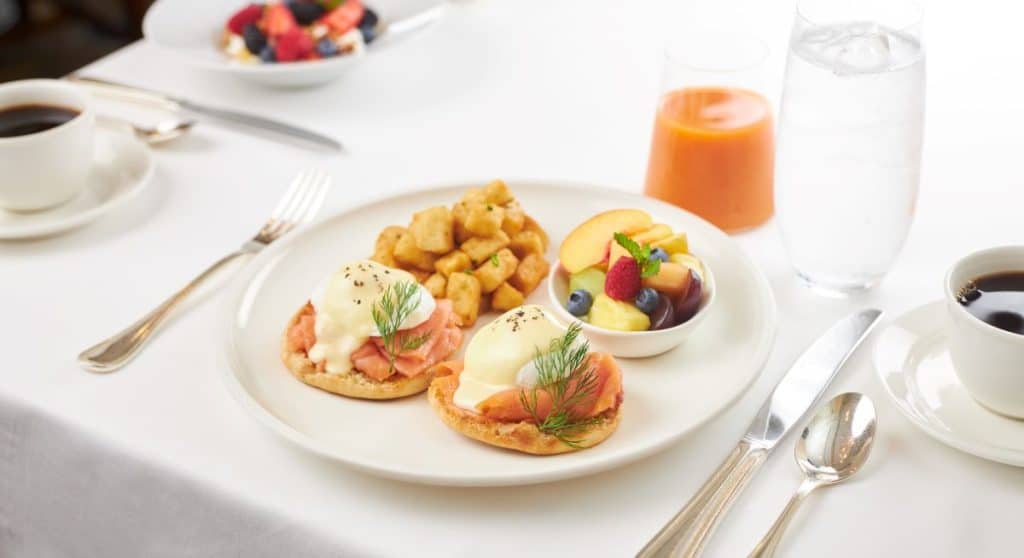 A picture of smoked royal salmon on muffins with a glass of juice behind the plate.