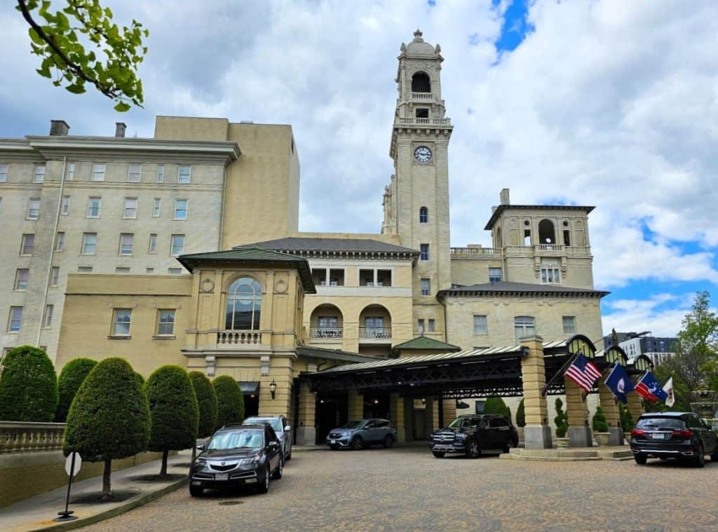 The large clock tower is part of the history of The Jefferson Hotel in Richmond Va. The building is massive and yellow, with a car parked in front.