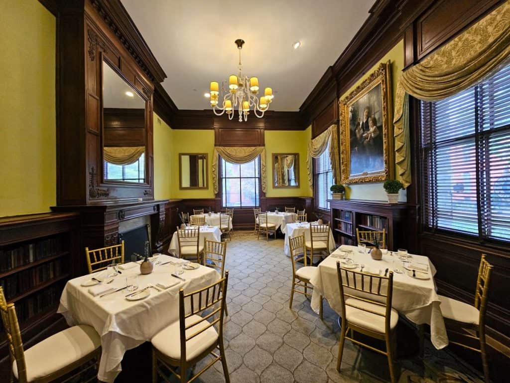 The library dining room at The Jefferson Hotel shows white tablelclothed tables with a chandelier hanging above.