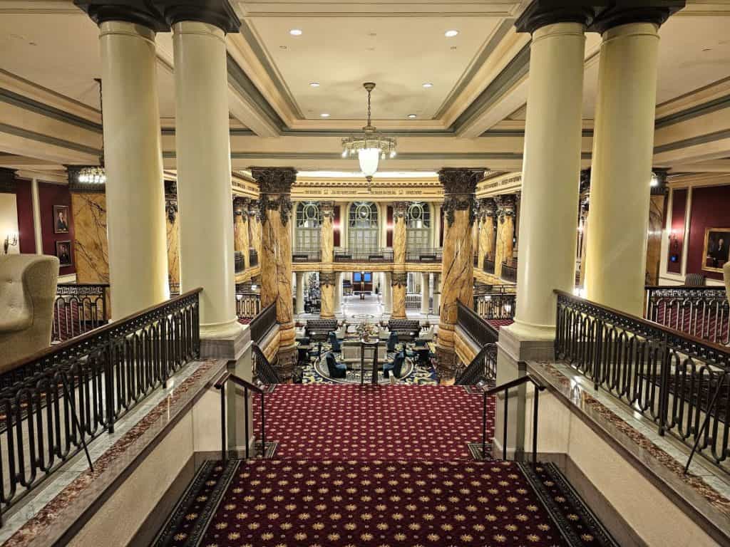 POV from the top of the Grand staircase at The Jefferson Hotel in Richmond with red carpet and white pillars.