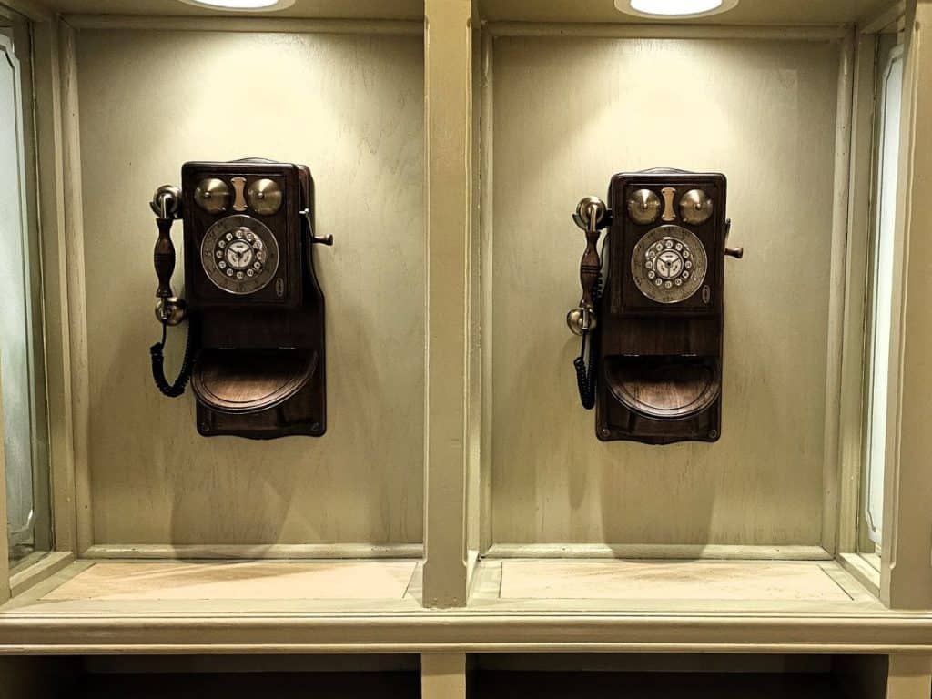 Two old rotary phones that are black, hang against beige walls at The Jefferson Hotel.