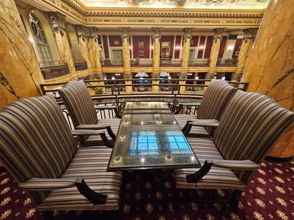 Four comfortable looking gray chairs sit around a table with the elaborate pillars of the Jefferson Hotel in the background.