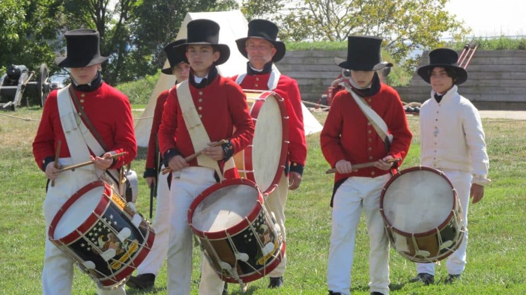 Young drummer boys wearing red shirts, black hats and white pants, portray a colonial band at Fort McHenry.
