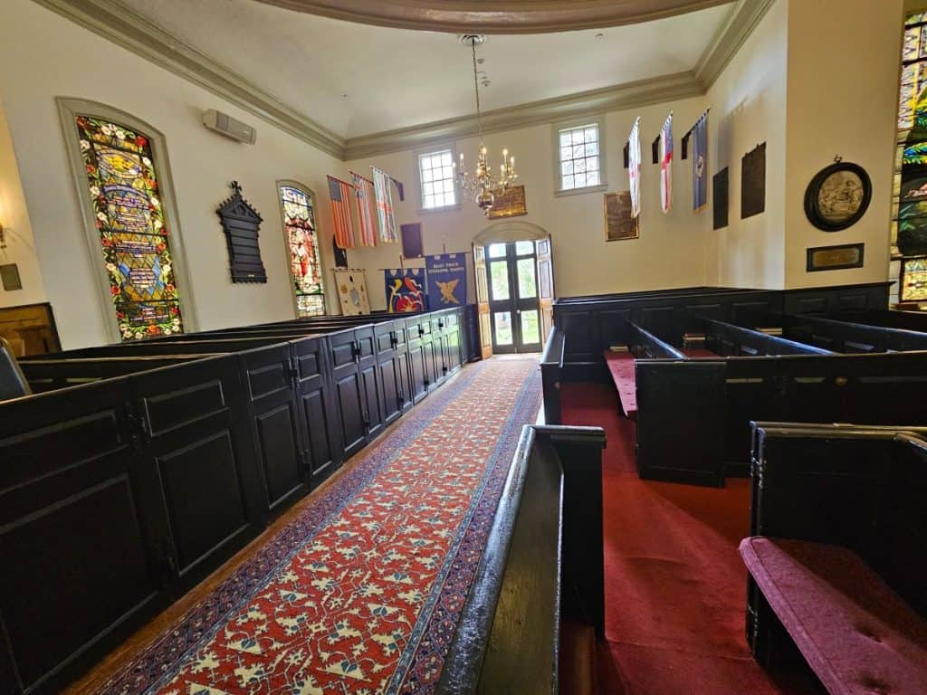 A red and gold carpet leads to a door with pews on each side at St. John's Church in Richmond.