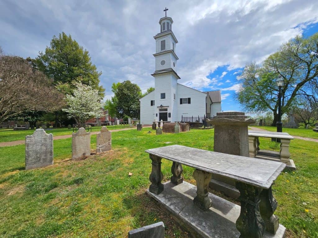 The white wooden structure of St John's Church in Richmond against a cloudy sky with tombstones in the front.