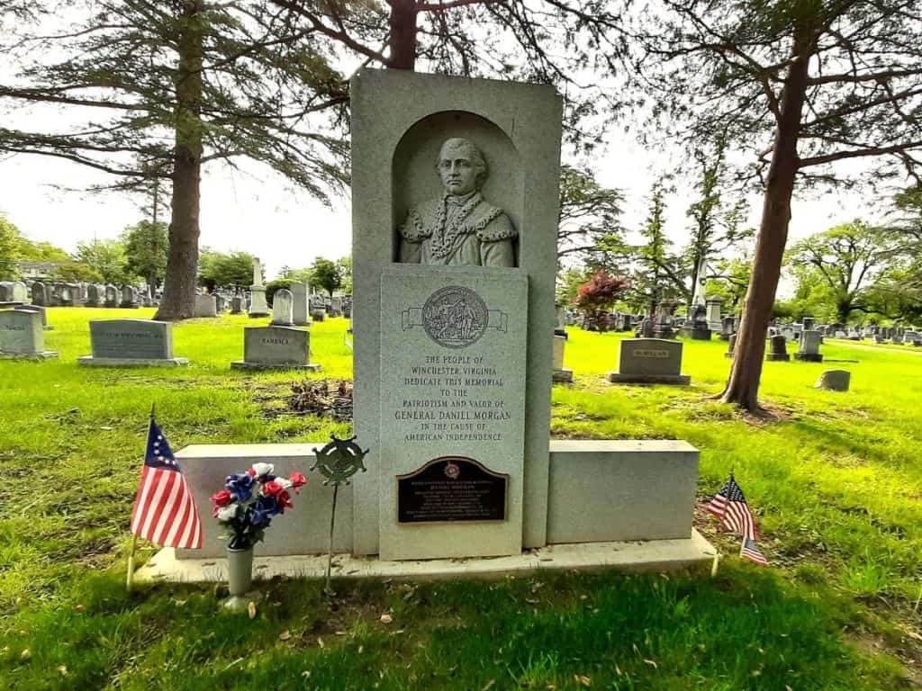 The tombstone of Revolutionary War hero General Daniel Morgan with his face engraved in stone and an American flag.