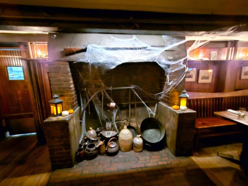 Cobwebs sweep across the mouth of a fireplace with old pots and pans in the fire area.