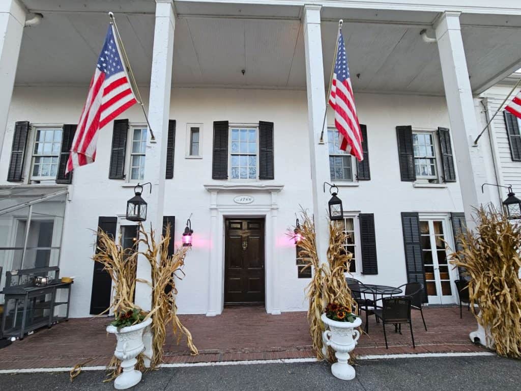A white building with black shutters and two american flags hanging on large white posts.