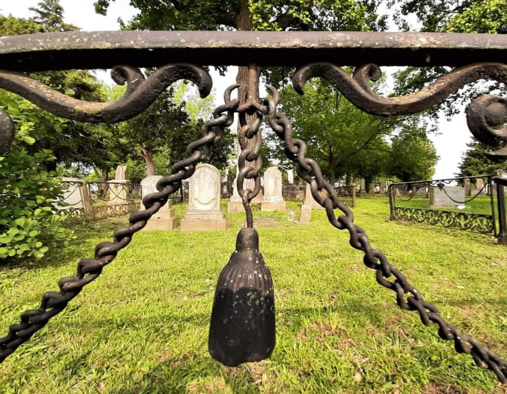 An iron bell and chain hangs from a fence surrounding graves.