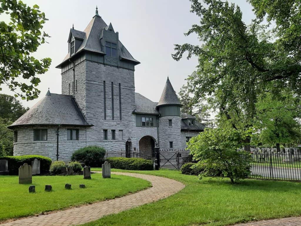 A gothic looking gray building with a brick pathway serves as the entrance to the Mount Hebron Cemetery in Winchester VA.