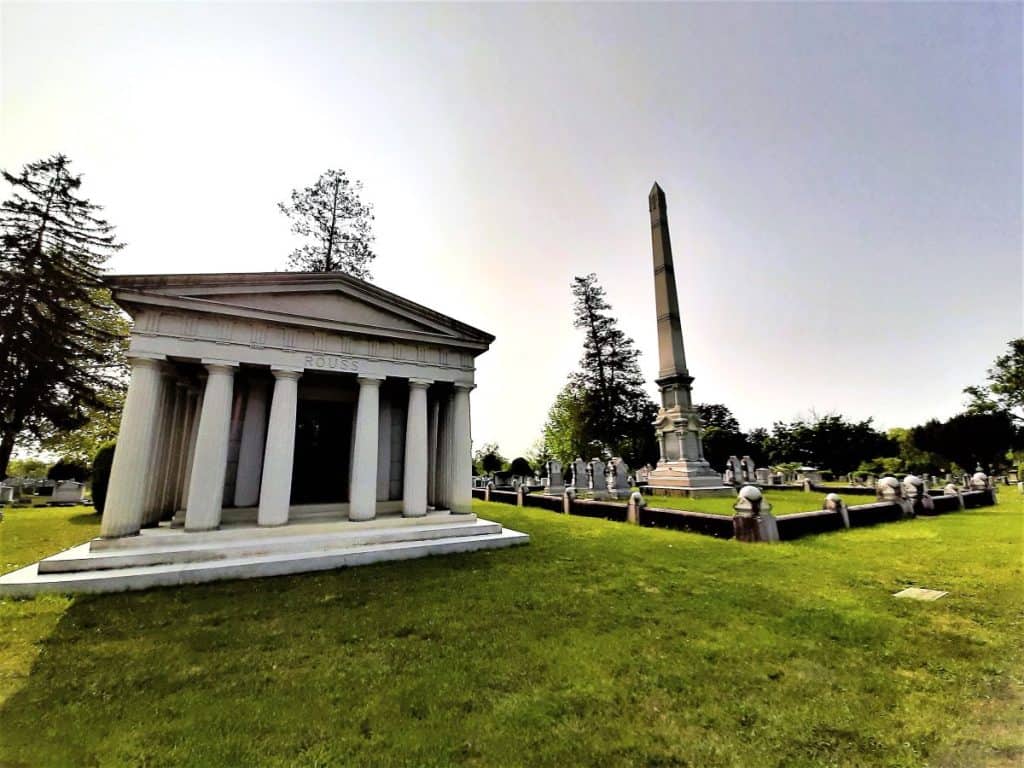 A white tomb with six pillars stands beside a family resting place with a tall marker.