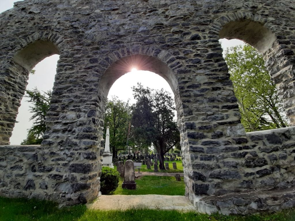 A stone arch of the Old Church Wall with the sun glimmering through. 