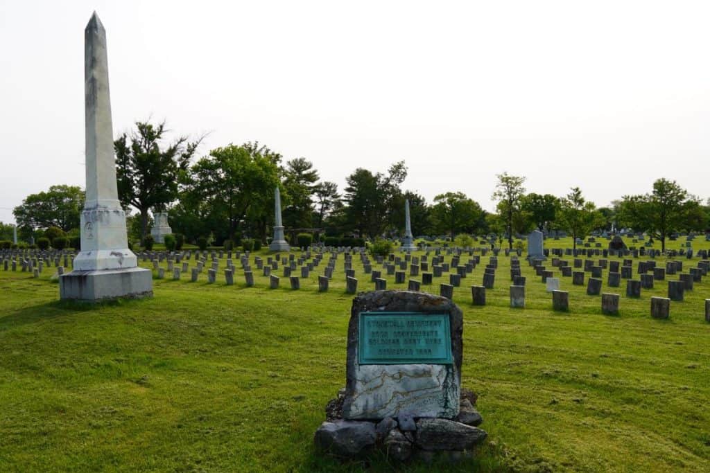 A stone that says Stonewall Cemetery, with rows of graves laid out behind it and a tall white statue in front.