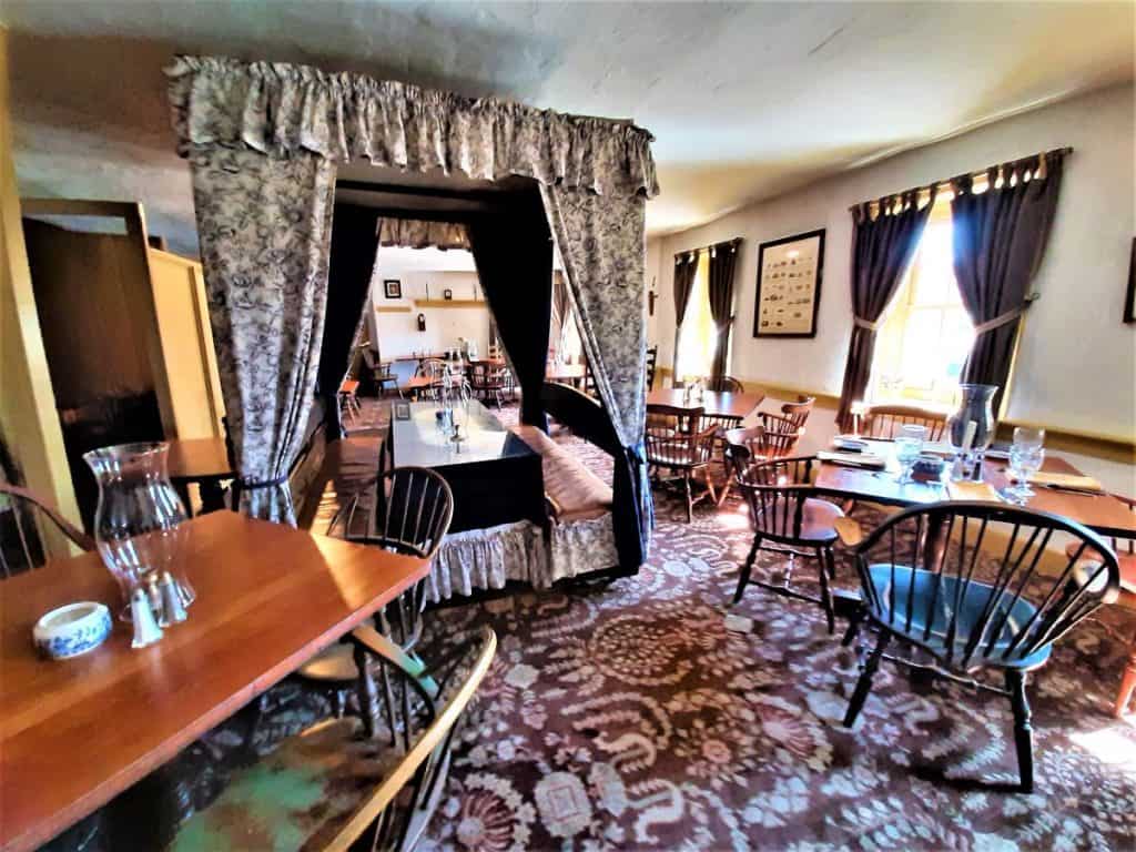 A table with a bed canopy over top with rich carpet on the floor and other tables in the foreground.