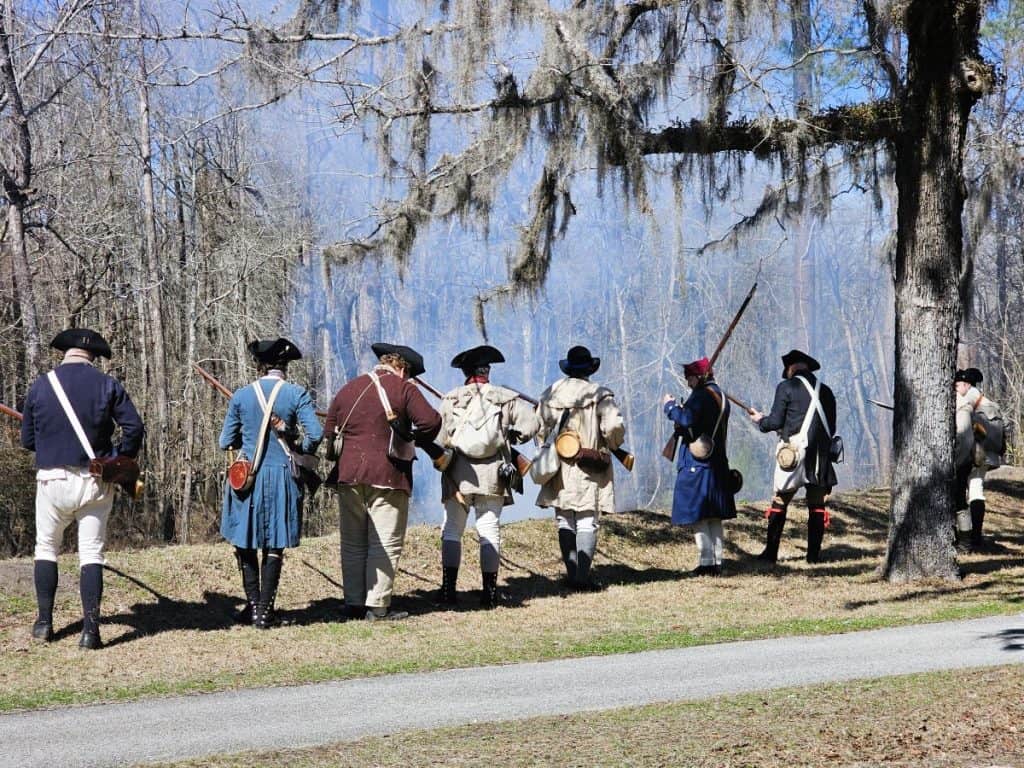 Soldiers in colonial dress stand in a haze after firing their weapons at Moore's Creek Battlefield.