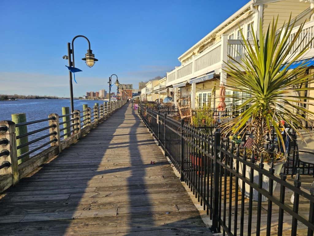 A wooden boardwalk on the water with buildings on the right and a lamp post on the left.