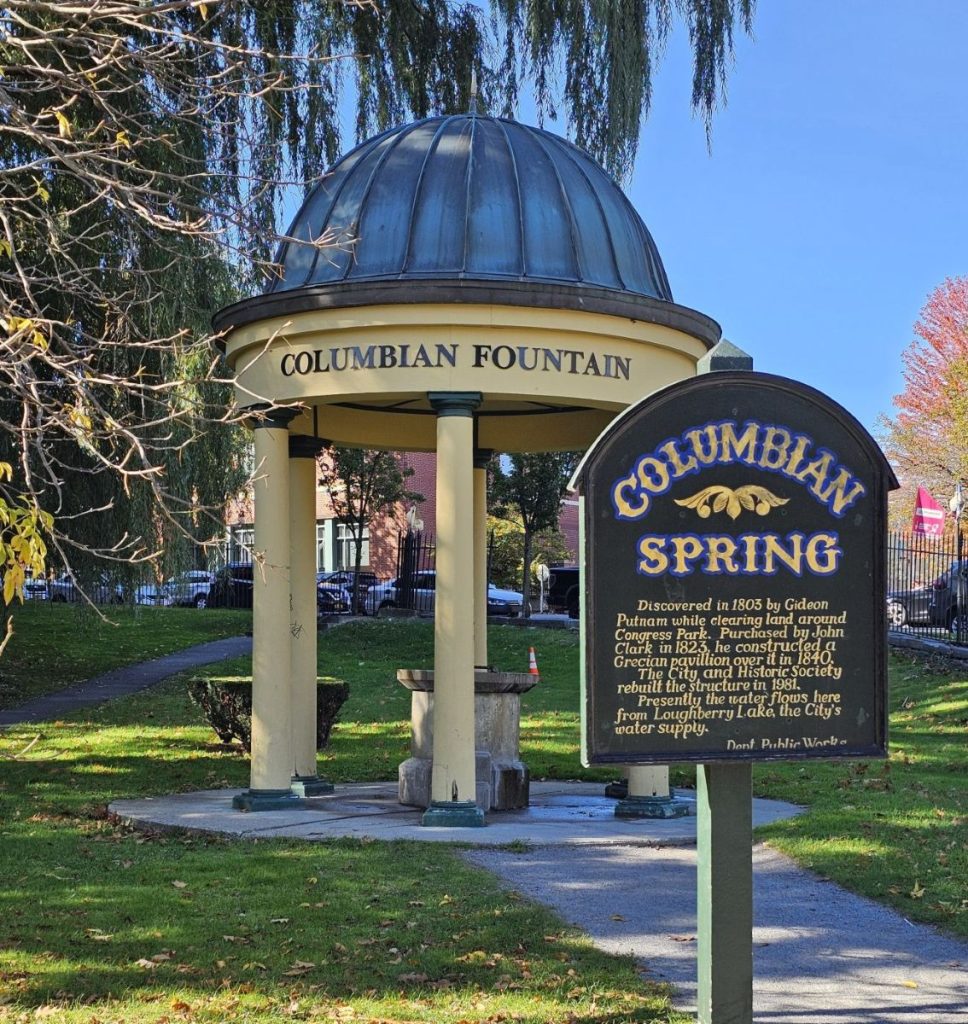 A sign that says Columbian Springs and a domed structure showing the Saratoga Springs natural mineral water fountain.