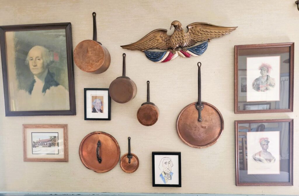 A wall in the 76 House showing a portrait of Washington and an eagle and a display of pans.