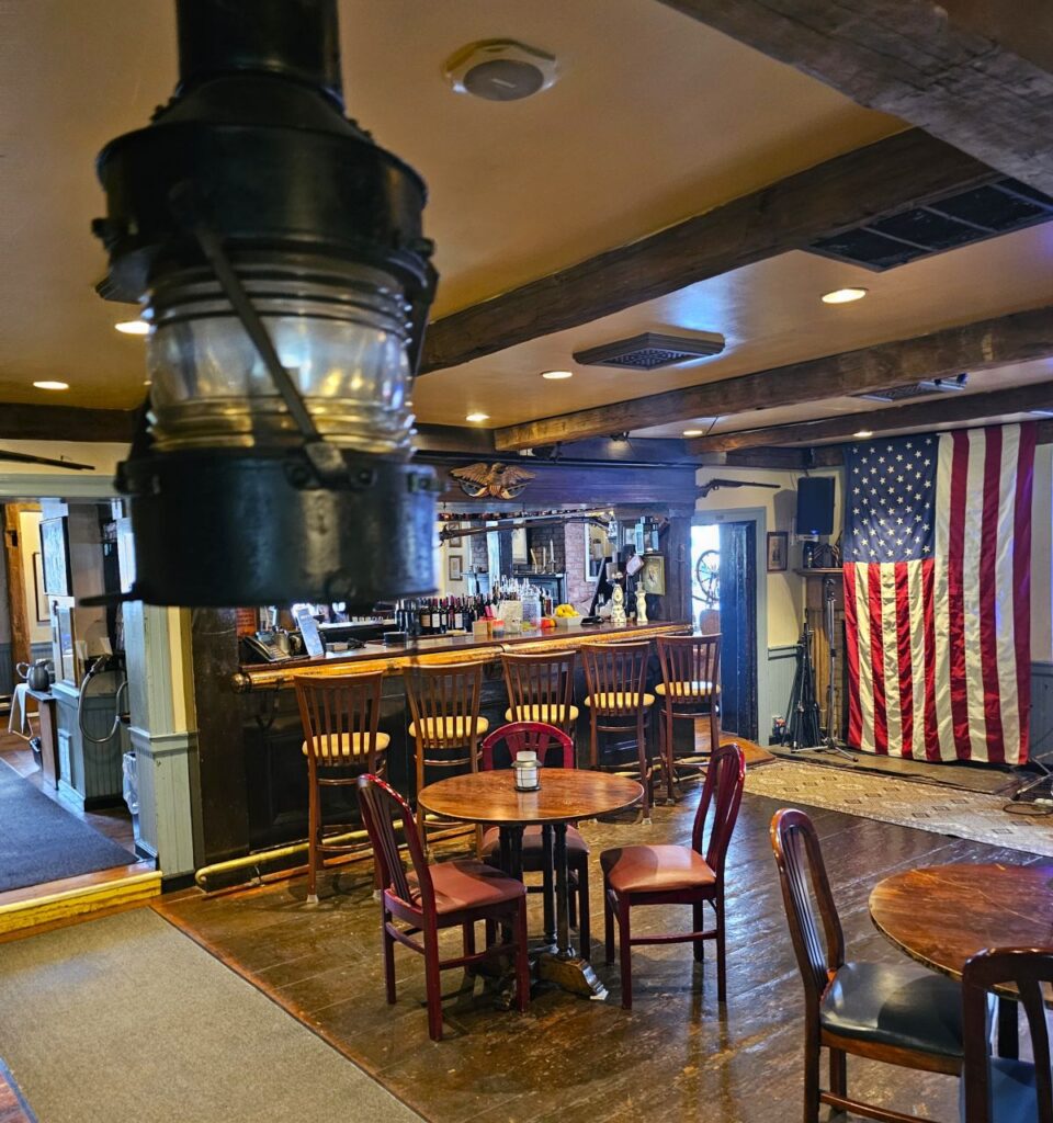 A flag hangs in the background of the Revolutionary War Tavern in Tappan, NY, with a lantern hanging in the foreground.
